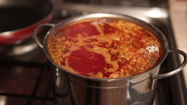 Close-up of a red Ukrainian borsch - tasty dish made with vegetables and meat boiling on a stove. 