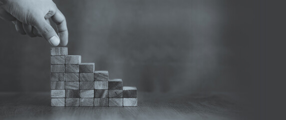 Hand is placing wood block tower stack in pyramid stair step with caution to prevent collapse or...