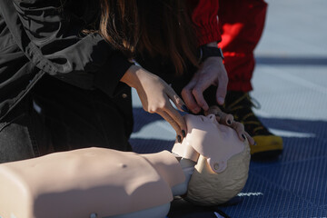 Details with the hands of a female student learning how to perform cardiopulmonary resuscitation (CPR) on a mannequin for educational purposes.
