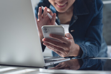 Close up of young asian business woman using mobile phone making video call via online meeting app during working on laptop computer from home office.