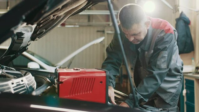 Car Mechanic Working In Auto Repair Service. Auto Electrician Troubleshooting A Car Engine. Electrician Working On Car Engine. Testing Electrical System On Automobile. Automobile Diagnosis