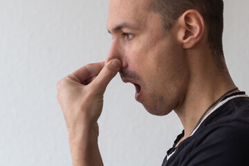 Man smells something stinky and pinches his nose to stop the bad odor - obrazy, fototapety, plakaty