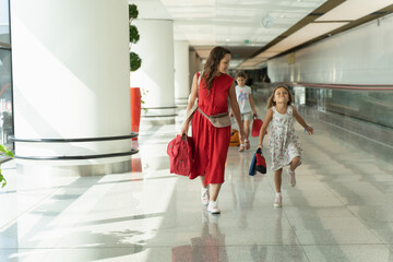 Happy family with suitcase is going on passageway to the airplane. Mom and daughters walk along the...