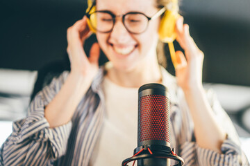 Positive woman with microphone recording podcast at studio.