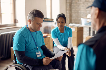 Volunteer coordinator in wheelchair going through checklist with his team at donation center.