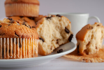 Muffins with chocolate chip on a white plate with awhite cup of coffee in the background.