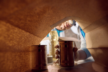 Close up of food bank volunteers packing donated food into paper bag.