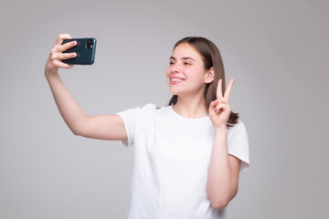 Portrait of woman using mobile phone. Girl holding smartphone over gray background. Girl making taking selfie.