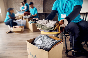Close up of man in wheelchair packing clothes in donation box while volunteering at community...