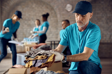 Mature man packing donated clothes in box while volunteering at charity center.