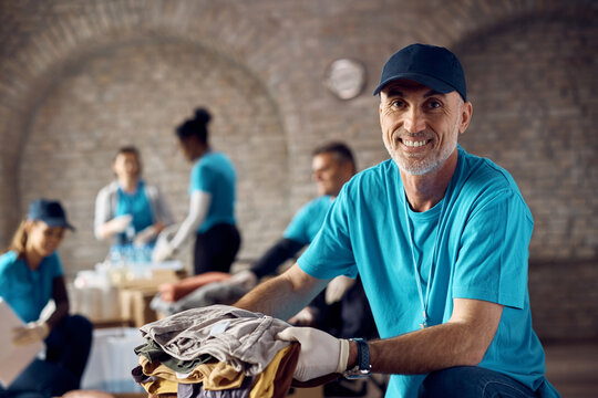 Happy Mature Volunteer Packing Clothes In Donation Boxes And Looking At Camera.