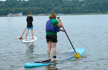 Old woman and a young boy rowing SUP board on the water