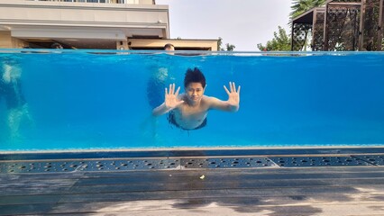 Portrait of asian boy underwater in swimming pool with glass wall. Happy handsome boy in mask dive...