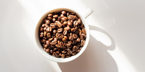Coffee beans in a white ceramic cup on a yellow background. Hard sun shadows. Top view