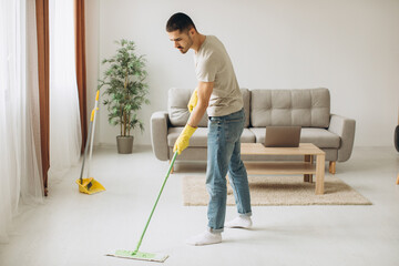 Young man washes the floor with a mop in the room