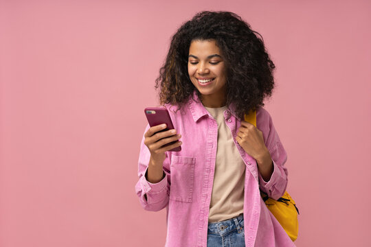 Smiling African American woman using mobile phone shopping online, reading text message isolated on pink background, copy space 