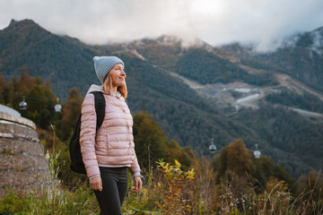 young woman smiling with a backpack in a hat, admiring looks at the mountains.