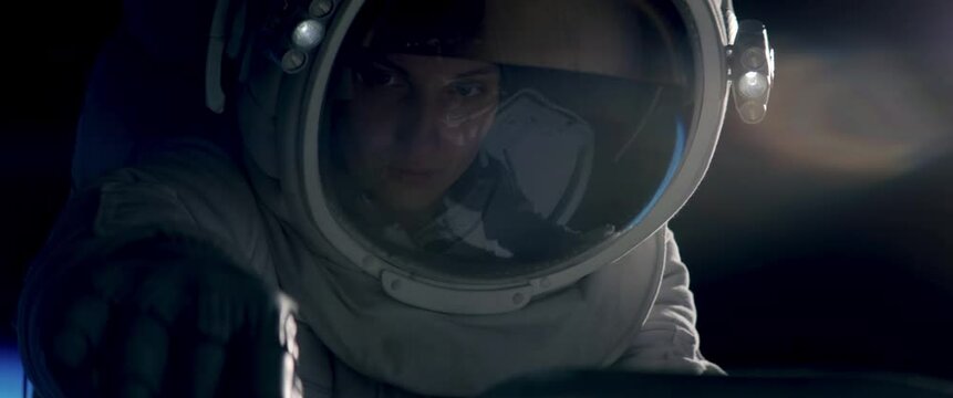 Female astronaut performing spacewalk, working on a outer part of a space craft. Shot with 2x anamorphic lens