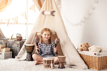 Little girl playing in room with maracas and djembe drums in kids wigwam © Ievgen Skrypko