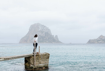 woman holding on to a pole over a rock in the mediterranean sea. girl feels free in IBIZA. she...