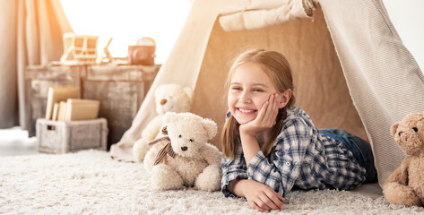 Little girl lying in wigwam with plush teddies in light room
