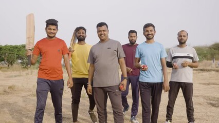 Team of cricket players with bat and ball coming and standing by looking at camera on field - concpet of competition, champions and active lifestyle.