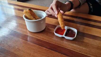 hands dipping chicken sticks in a bowl of tomato sauce, ketchup and mayonnaise.Hand hold chicken stick fried dip sauce on white plate. 