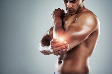 No lifting weights for a while. Cropped shot of a sporty young man holding his elbow in pain...