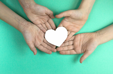 Fototapeta premium In the hands of children, a heart cut out of paper on a light green background. Children dream of peace and love concept. Child love. selective focus