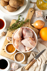 Raw chicken legs, potatoes and spices on a light gray culinary background. Raw poultry meat, vegetables and seasonings are prepared for pickling. Top view	