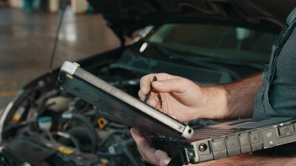 Auto service, maintenance concept. Close up of hands car electrician repairs car. Mechanic use notebook computers to record engine checks collect detailed information during work