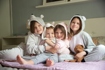 Four girls girlfriends sisters in pajamas at home on the bed, a pajama party in soft amigurumi costumes in a light gray bedroom, four children girls hugging on the bed