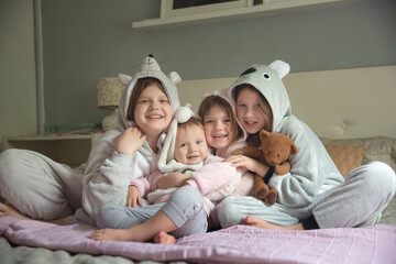 Four girls girlfriends sisters in pajamas at home on the bed, a pajama party in soft amigurumi costumes in a light gray bedroom, four children girls hugging on the bed