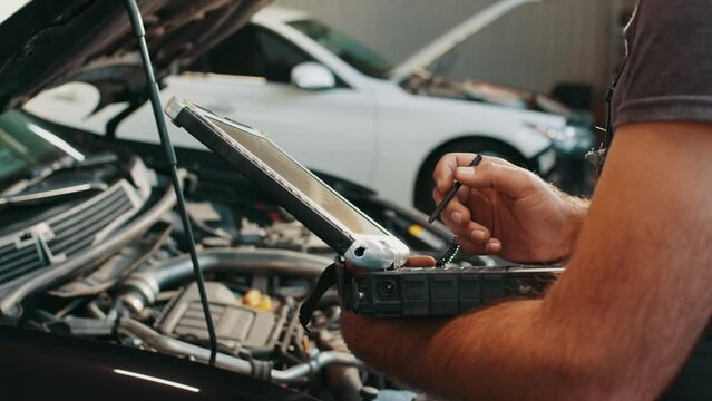 Hands of mechanic working in auto repair shop. Car electrician repairs car. Mechanic use notebook computers to record engine checks collect detailed information during work