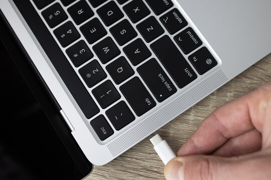 Connect the usb type-c cable to the computer. Connecting the usb type-c cable to the charging connector close-up. A man connects usb type-c cable to a laptop connector.