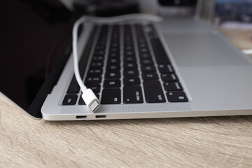 Charging battery laptop. Modern USB C port for fast charge. White cable plugged in laptop close-up view