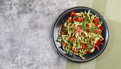 Cucumbers, bell pepper and herbs fresh healthy salad  on a round plate on a dark gray background. Top view, flat lay