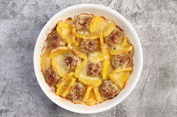 Potato with meatballs in a white baking dish on a dark grey background. Top view, flat lay