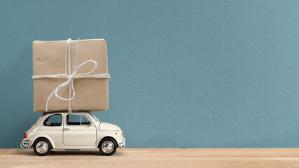 Retro white toy car delivering gift box atop on blue background