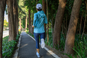 Fitness woman running training for marathon on sunny tropical park trail