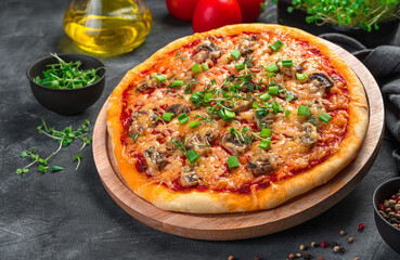 Pizza with cheese, mushrooms, tomatoes and herbs on a wooden board on a dark background.