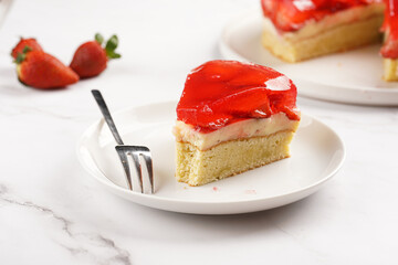 a Piece of a three-layered cake with vanilla pudding, strawberry jelly and fresh strawberries on a white marble background