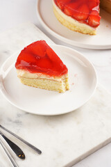 a Piece of a three-layered cake with vanilla pudding, strawberry jelly and fresh strawberries on a white marble background