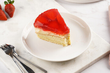 a Piece of a three-layered cake with vanilla pudding, strawberry jelly and fresh strawberries on a white marble background