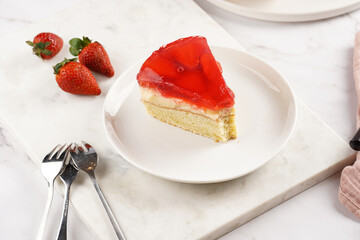 a Piece of a three-layered cake with vanilla pudding, strawberry jelly and fresh strawberries on a white marble background