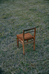 wooden chair with brown upholstery stands at sunset in a field of grass