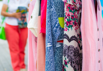 Clothes hanging on a rail at a street market outdoors. Colorful clothes for sale by a street vendor