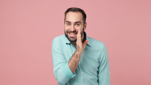 Secret young brunet man 20s years old wears blue shirt whispering gossip and tells secret behind her hand sharing news isolated on plain plain pink background studio. People emotions lifestyle concept