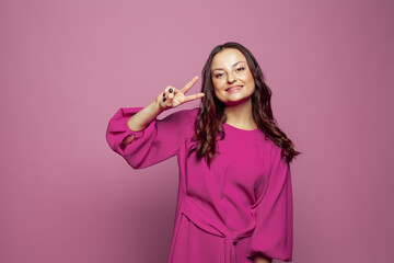 Pretty cheerful positive woman gesturing with fingers and smiling against pink wall studio background