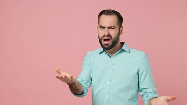 Side profile view shocked young brunet man 20s wears blue shirt looking camera spreading hands ask what why wave hand isolated on plain plain pink background studio. People emotions lifestyle concept